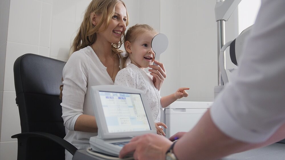 Woman helping her daughter with a pediatric eye exam.